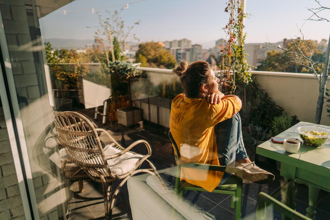 Una mujer sentada en su balcón considerando si alquilar o comprar una vivienda en Madrid