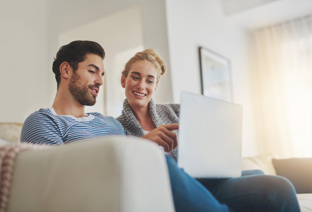 Una pareja sentada en un sofá mirando su portátil mientras lee sobre el trámite para vender una casa en Madrid